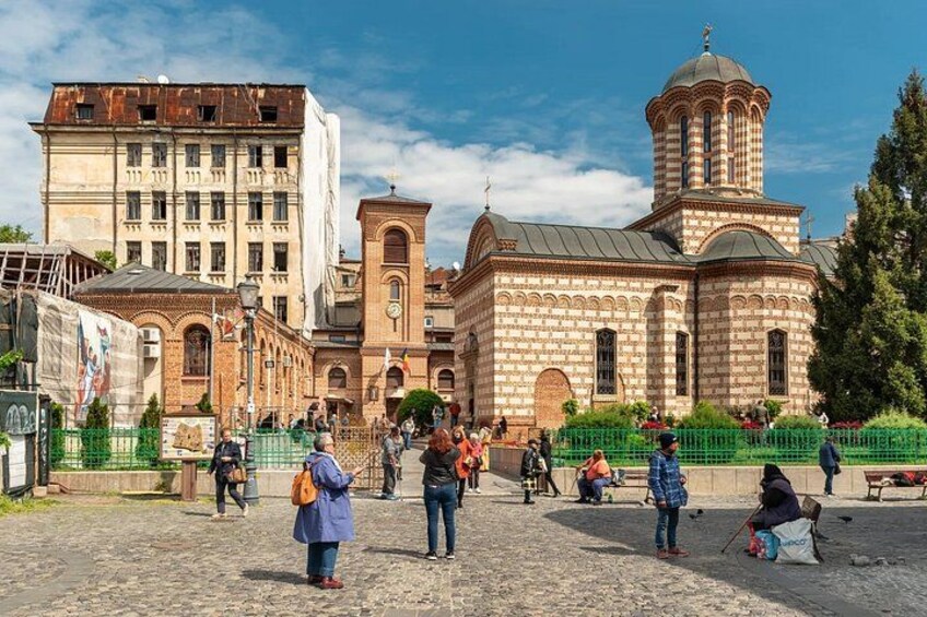 A historic building with a dome and arched windows, surrounded by a cobblestone plaza with people walking and sitting. 3