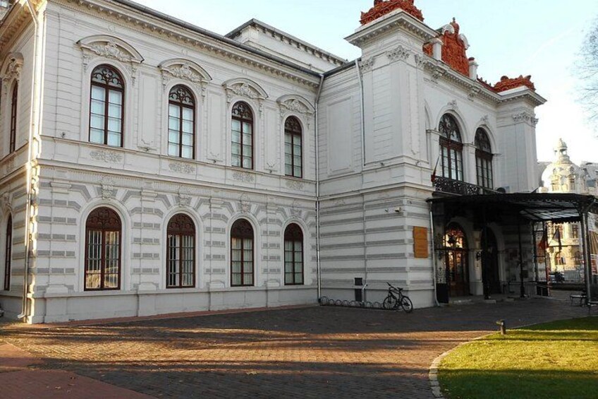 A white building with arched windows and a red roof, a bicycle, and a grassy area. 1