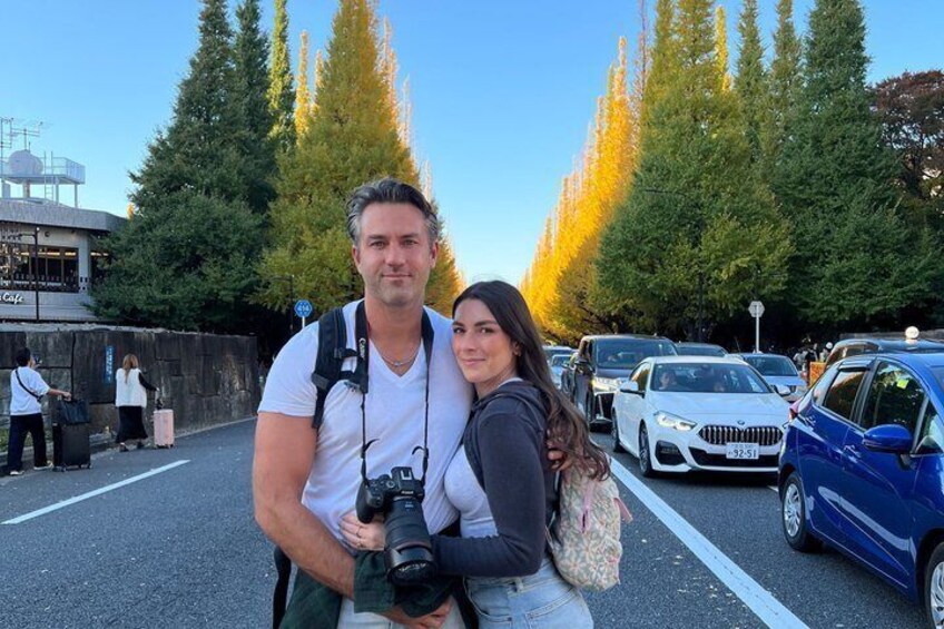 A man and woman standing in a parking lot with trees and a building in the background. 3
