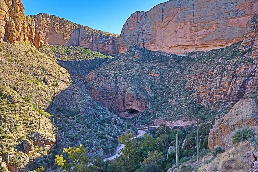 A canyon with a winding road, rocky cliffs, and sparse vegetation. 3