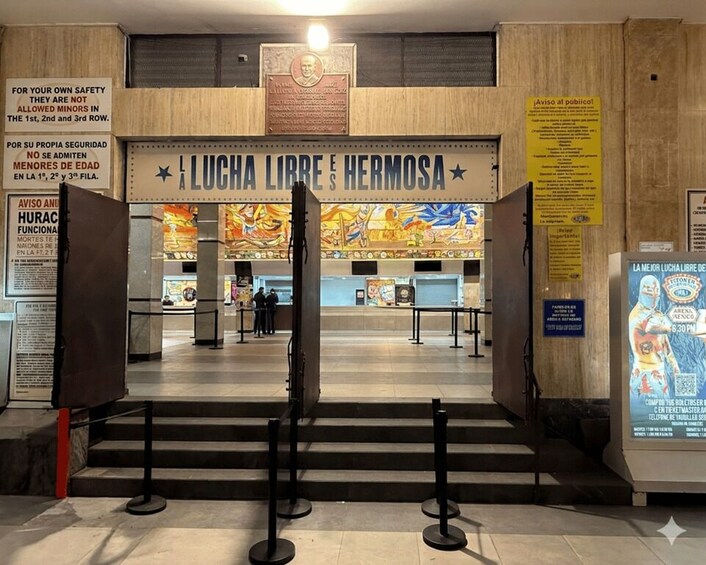 An entrance to a building with a sign reading 'LA LUCHA LIBRE E HERMOSA' and a mural in the background. 2