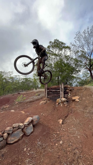 A person performing a bike stunt on a dirt trail with trees and a cloudy sky in the background. 1
