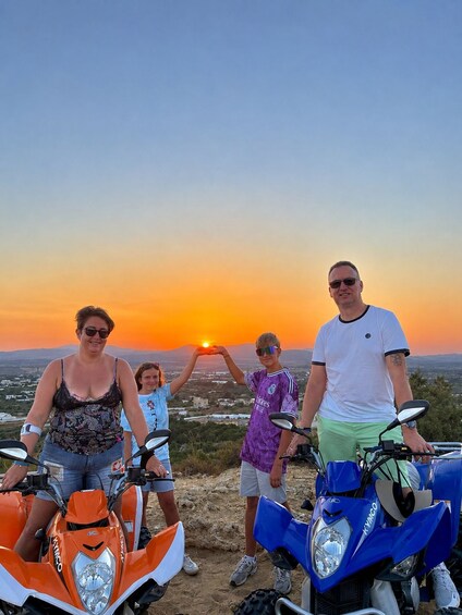 A sunset with four people and two quad bikes on a hill. 2