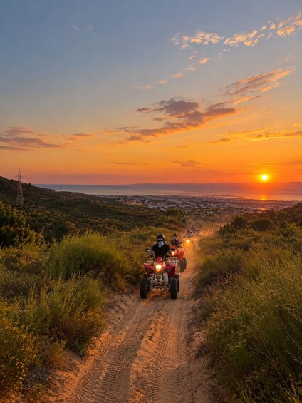 A sunset over a coastal landscape with a dirt path and people riding ATVs. 1