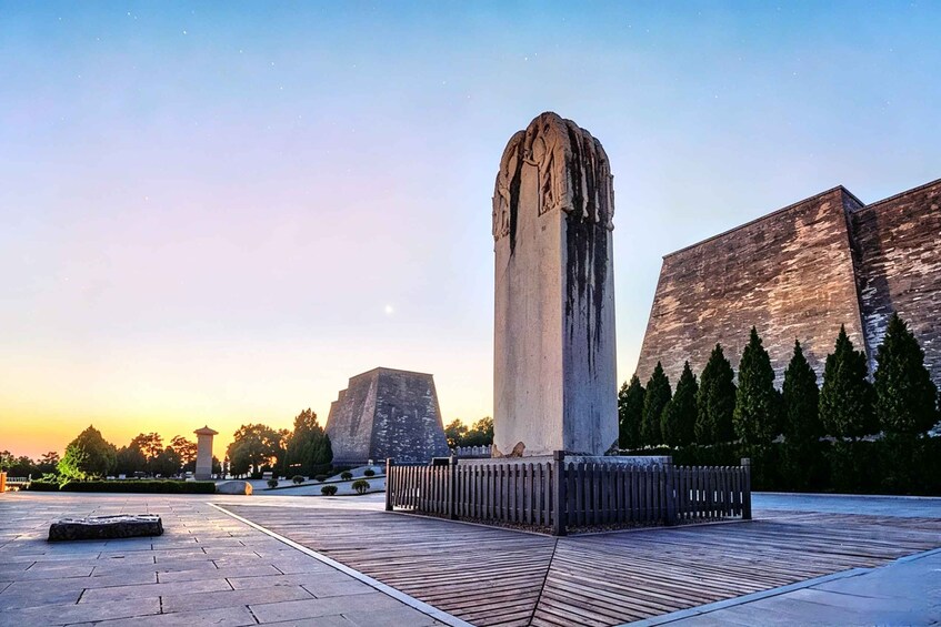 Korkea, sään kuluttama monumentti, suuri kivirakennelma taustalla ja puinen aita etualalla. 2