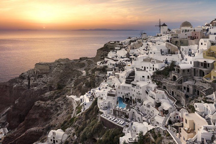 A coastal village with white buildings, a windmill, and a sunset. 2