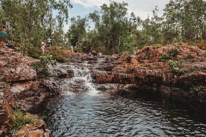 A natural landscape with a rocky waterfall, dense greenery, and a clear sky. 2