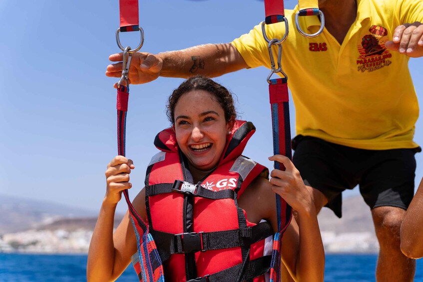 A person in a red life jacket holding onto a harness, with another person assisting. 3