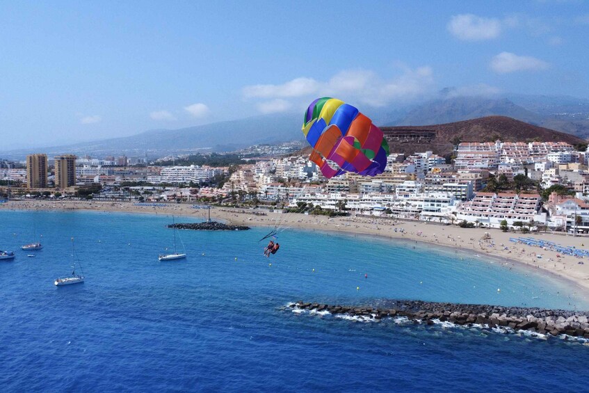 A coastal cityscape with a colorful parachute, boats, and a beach. 1