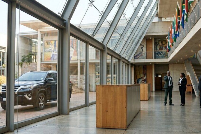 A modern building with large glass windows, a reception desk, and a staircase. Flags are displayed on the upper level. 4