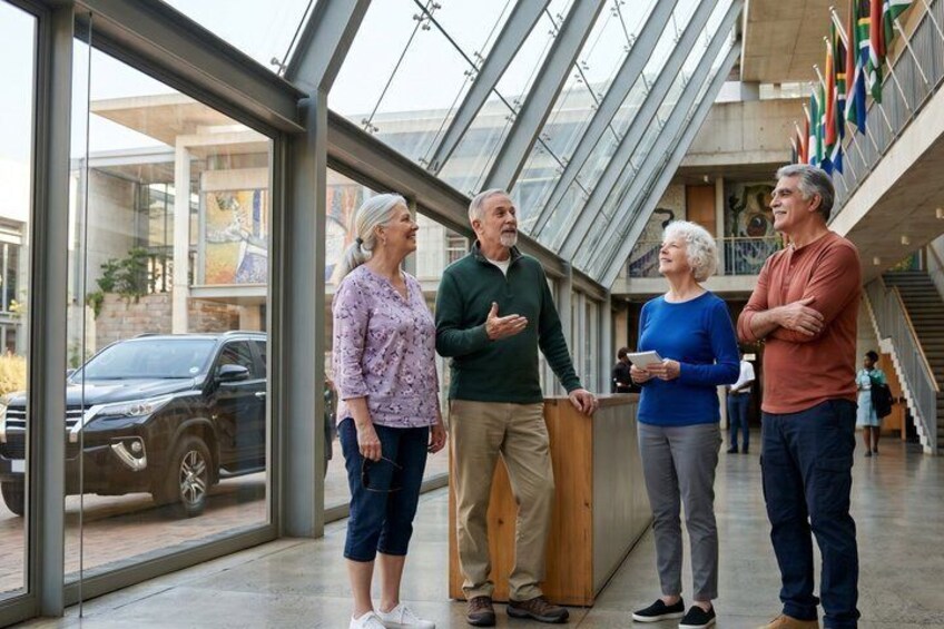 A group of people standing inside a building with large windows and a glass ceiling, looking outside. 3