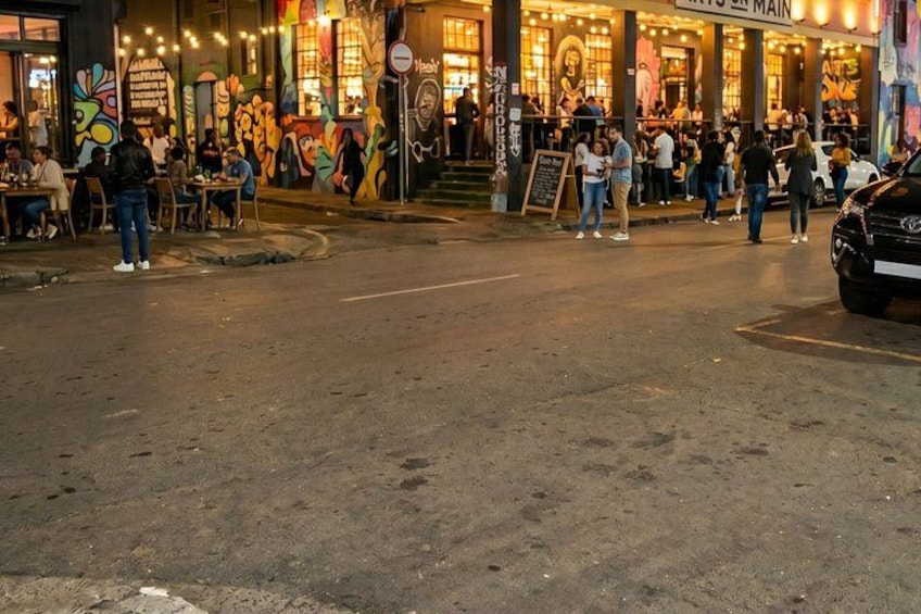 A street with a restaurant, people sitting outside, and a car parked on the side. 1