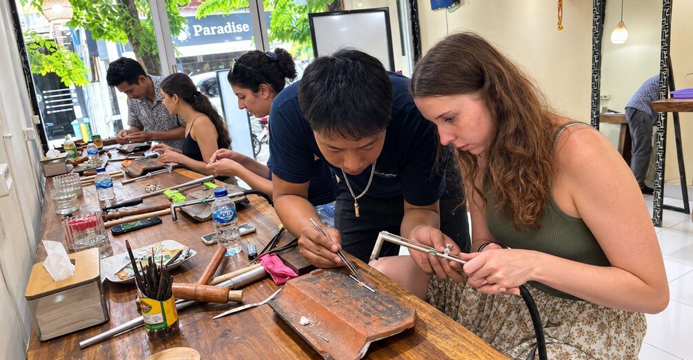 A group of people engaged in a craft activity, possibly pottery or woodworking, at a table with various tools and materials. 5