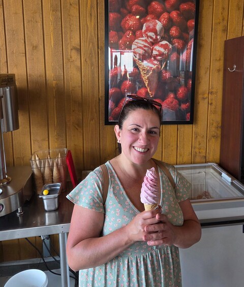 A person holding an ice cream cone in front of a wooden wall with a strawberry-themed poster. 3