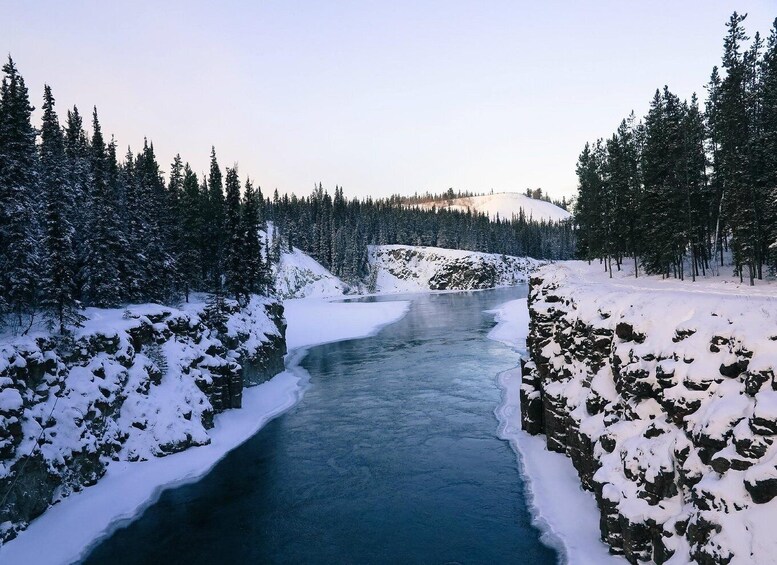A frozen river surrounded by snow-covered trees and rocky terrain. 5