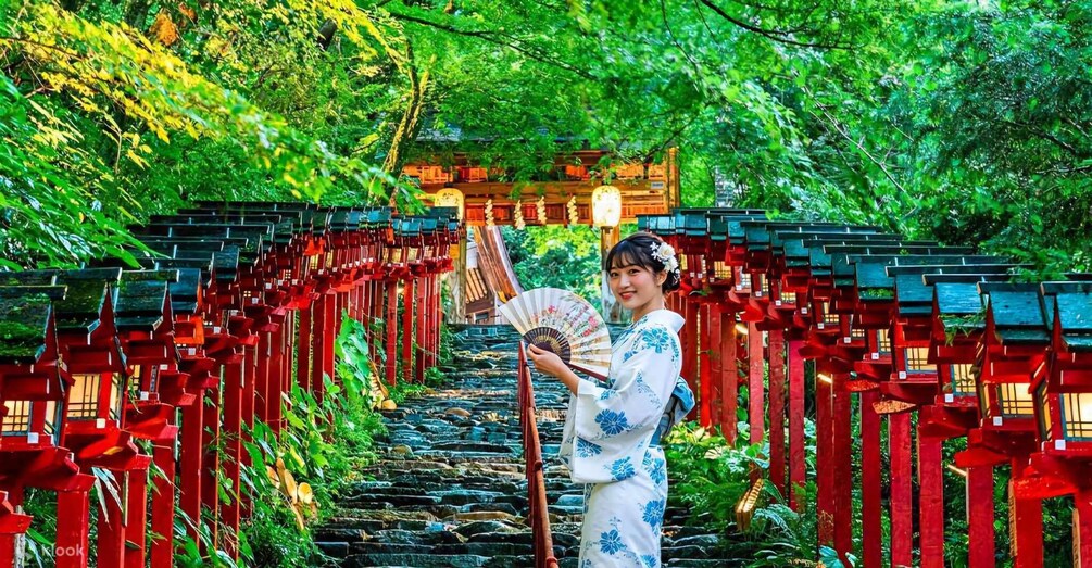 A person holding a fan in front of a traditional Japanese torii gate. 3
