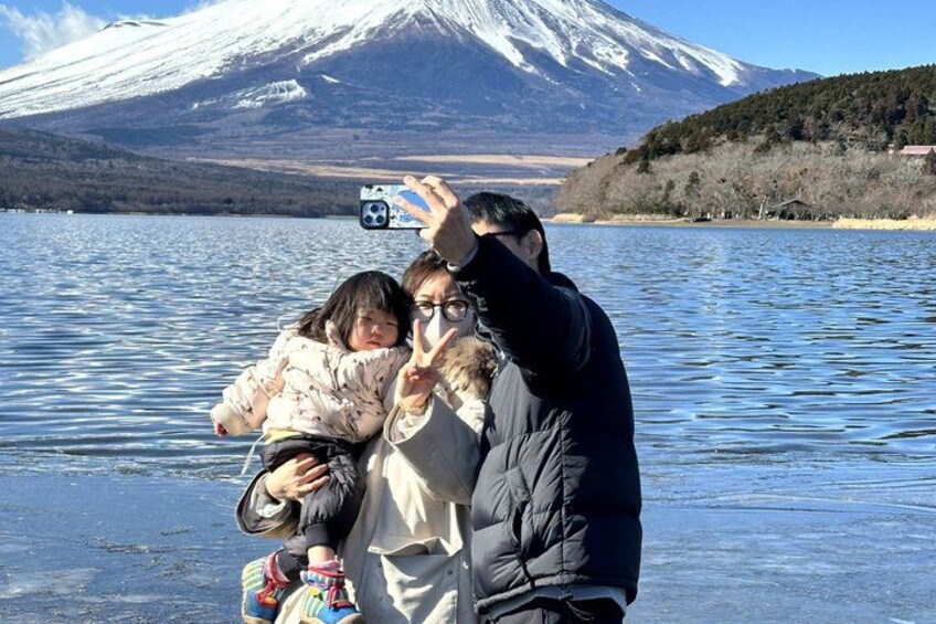 A person taking a selfie with a child by a lake with a snow-capped mountain in the background. 5
