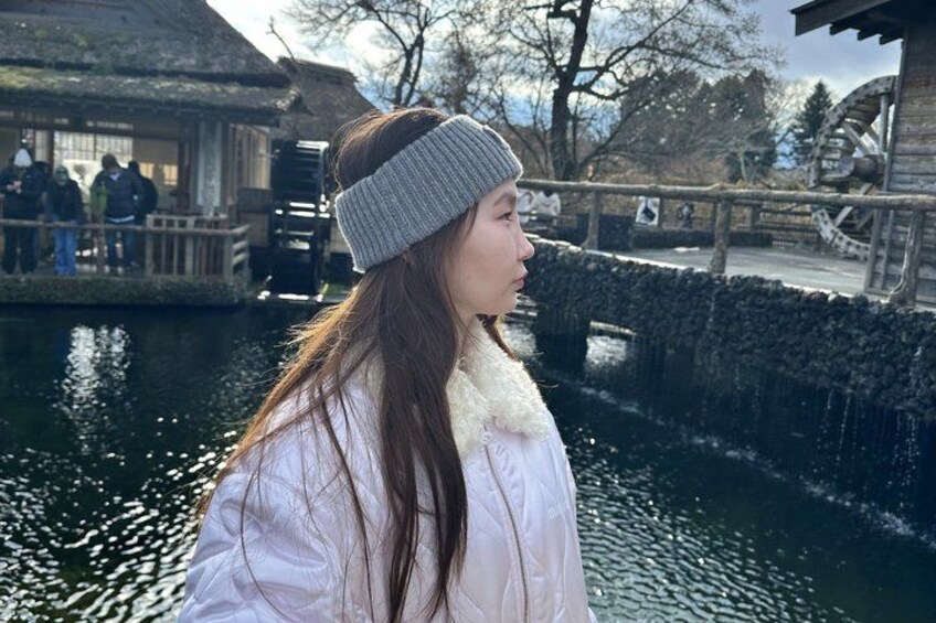 A person in a white coat and beanie near a water feature with a wooden structure in the background. 2