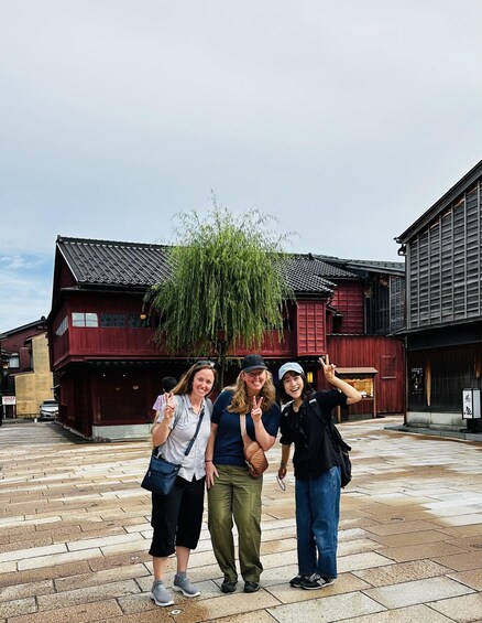 Three people posing in front of traditional Japanese buildings with a weeping willow tree. 1