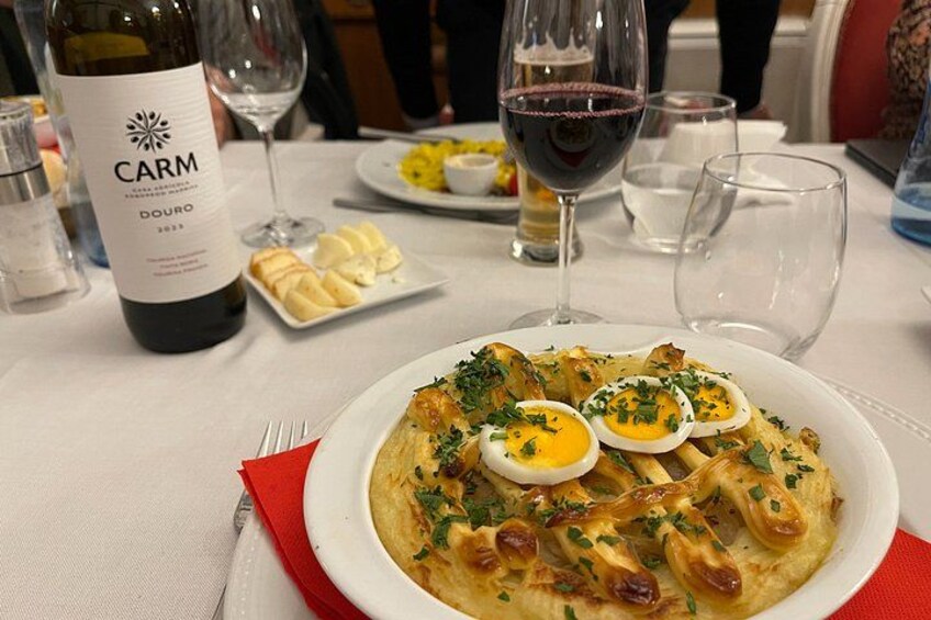 A plate of food with eggs and herbs, a bottle of wine, and glasses on a table. 2