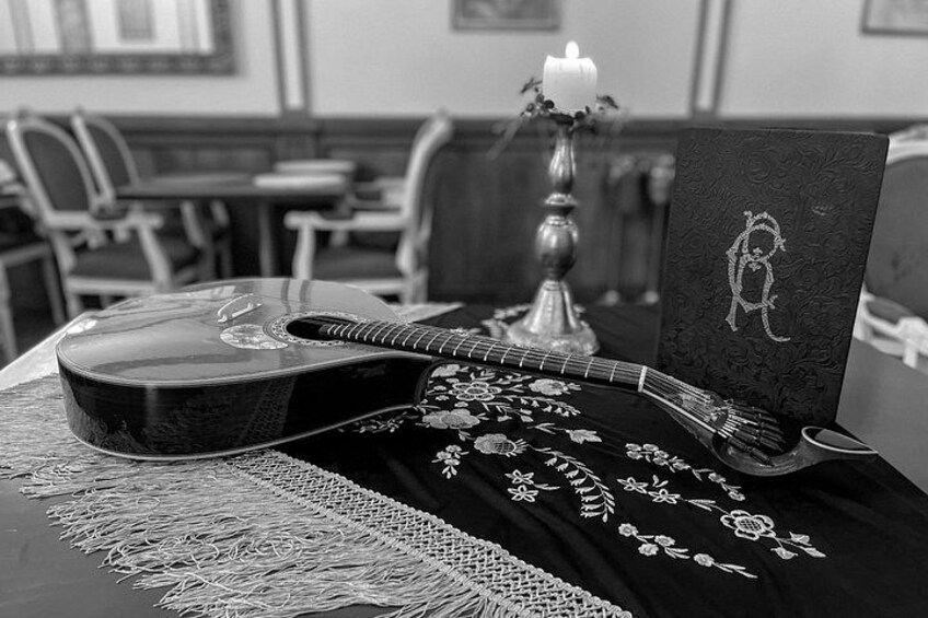 A black and white photo of a guitar, a candle, and a book on a table with a lace tablecloth. 3