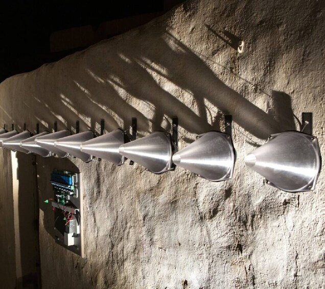 A row of metallic, conical objects mounted on a textured wall. 3