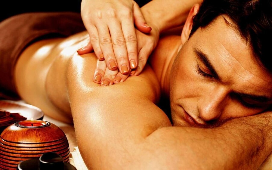 A person receiving a massage with hands on their back, a candle, and a wooden object on the table. 4