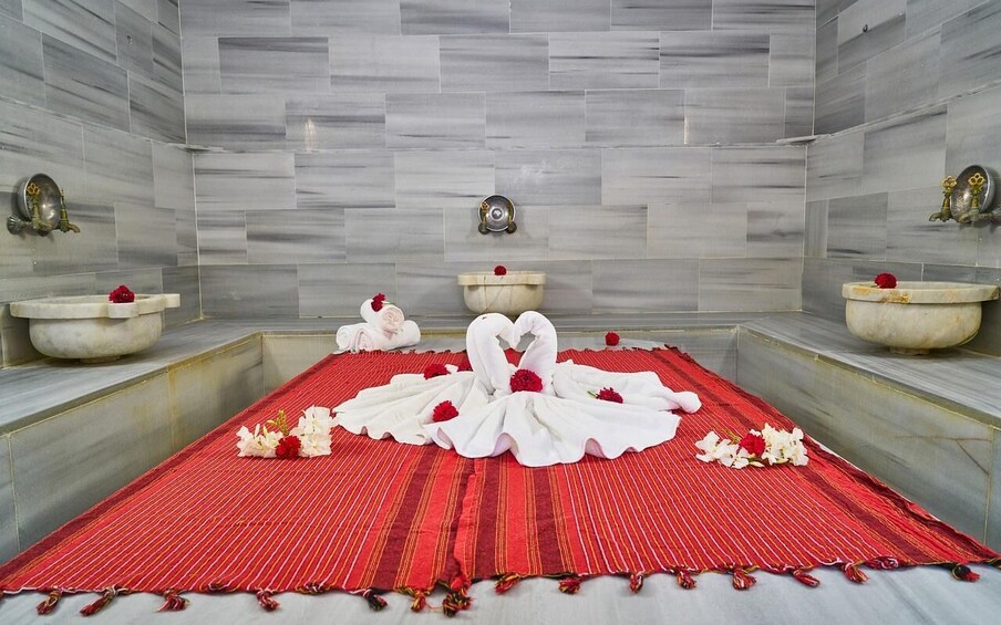 A bathroom with marble walls, a red mat, and two white swan-shaped towels. 3