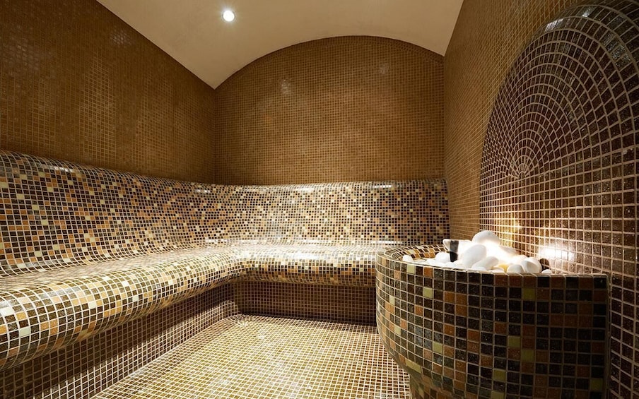A mosaic-tiled sauna with a curved bench and a small pool. 2