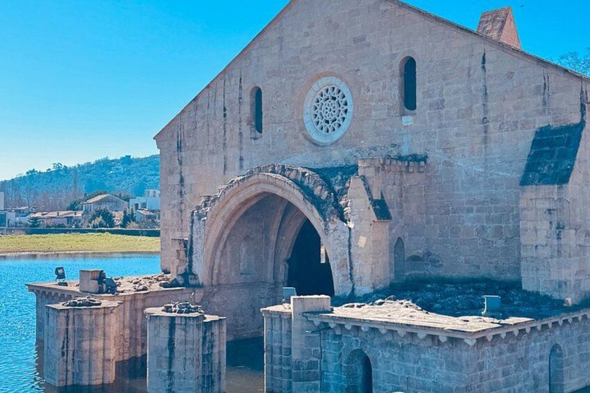 A historic stone building with a large arched entrance, a circular window, and a bridge extending into a body of water. 4