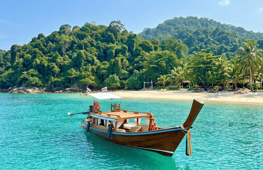 A wooden boat on turquoise water with a beach and palm trees in the background. 3