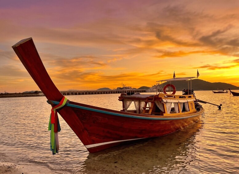 A traditional wooden boat with a red and blue hull, docked at a pier during sunset. 1