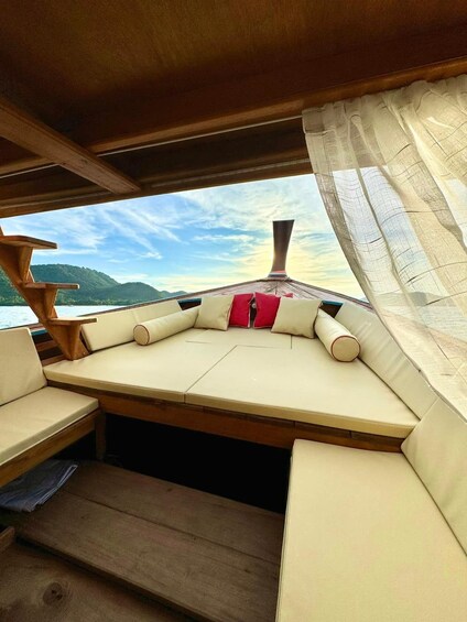 A boat's interior with a cushioned seating area, wooden deck, and a view of the water and hills. 4