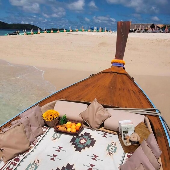 A boat's deck with a patterned tablecloth, cushions, a basket of fruits, and a small book. 4
