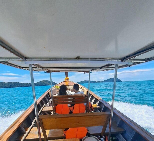 A boat with two passengers, a canopy, and a view of the sea and distant islands. 3