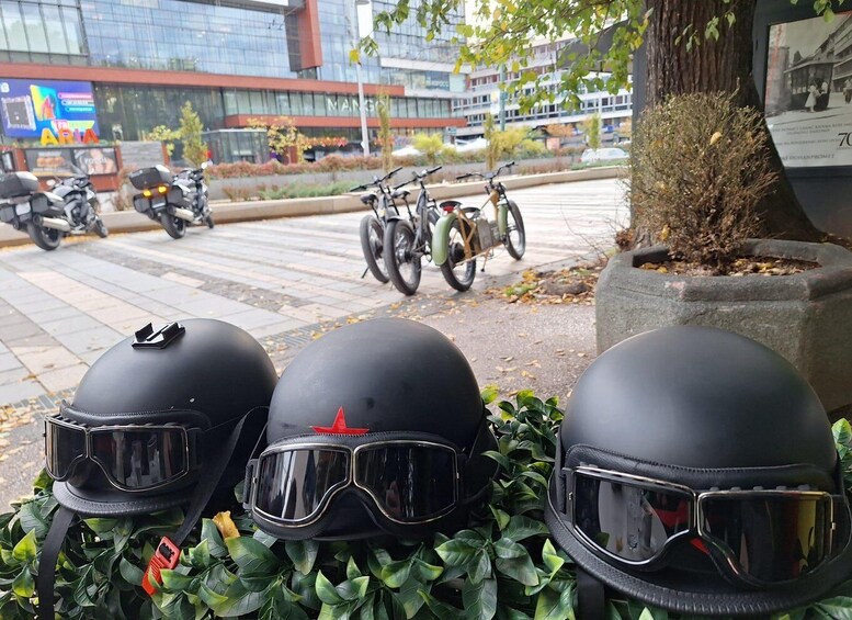 Three helmets on a ledge with greenery, a street with parked motorcycles and bicycles, and a building with 'MANGO' signage in the background. 4
