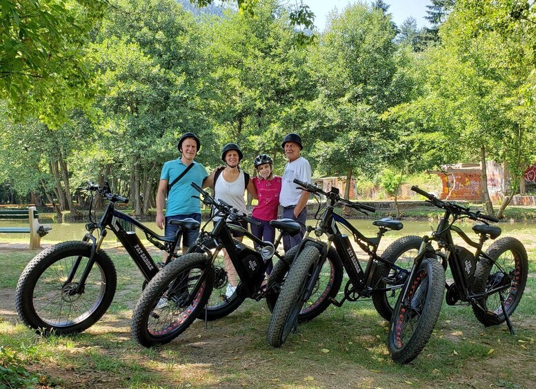 Four people standing with bicycles in a park with trees and a river. 1