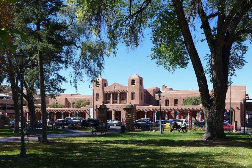 A building with a terracotta facade, surrounded by trees and a parking lot. 1