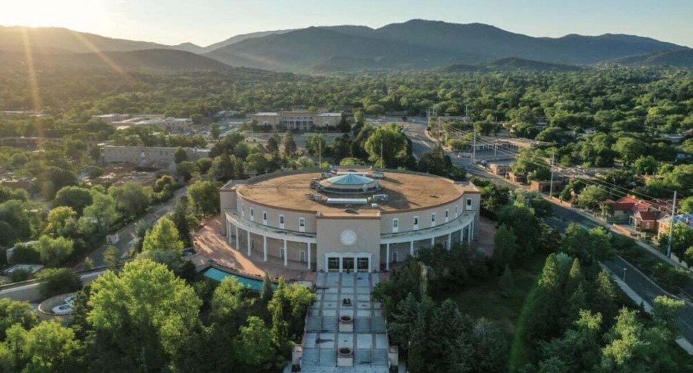 A circular building with a central dome, surrounded by trees and a mountainous backdrop. 2