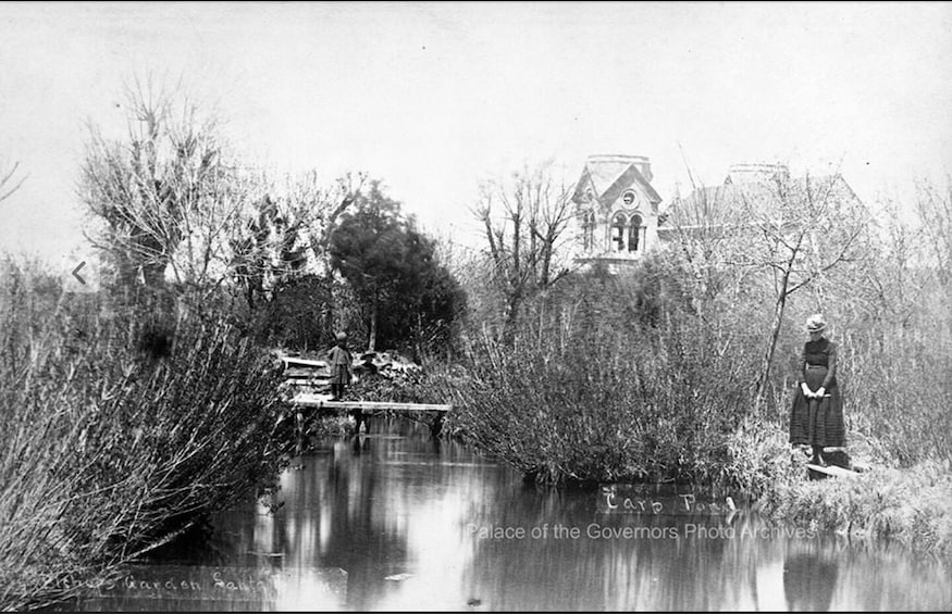 A wooden bridge over a body of water, surrounded by dense vegetation and a building with a clock tower in the background. 5