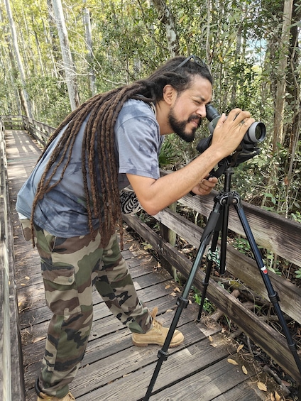 A person with dreadlocks using a telescope on a wooden bridge in a forest. 1