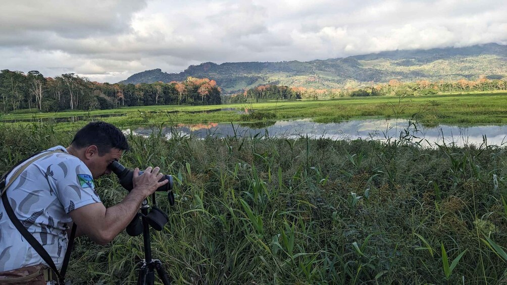 A person photographing a landscape with a pond, grass, and hills in the background. 5