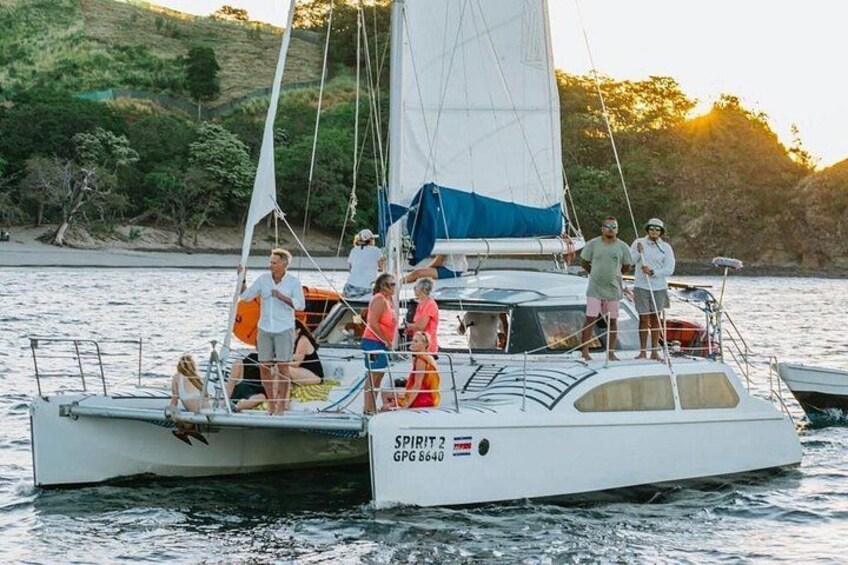 Un velero llamado 'SPIRIT 2' con personas a bordo navegando sobre aguas tranquilas, con un paisaje montañoso al fondo. 5