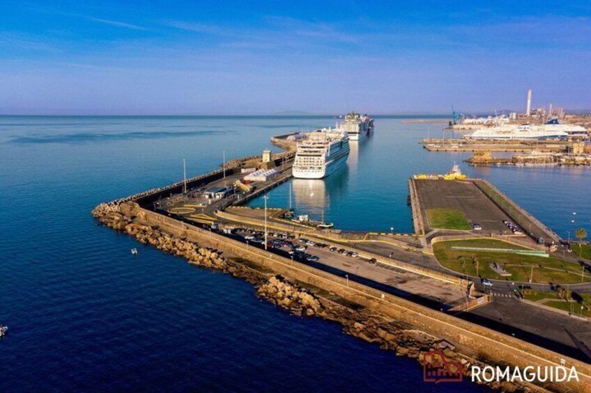 A coastal port with a large cruise ship docked, a breakwater, and a clear sky. 1