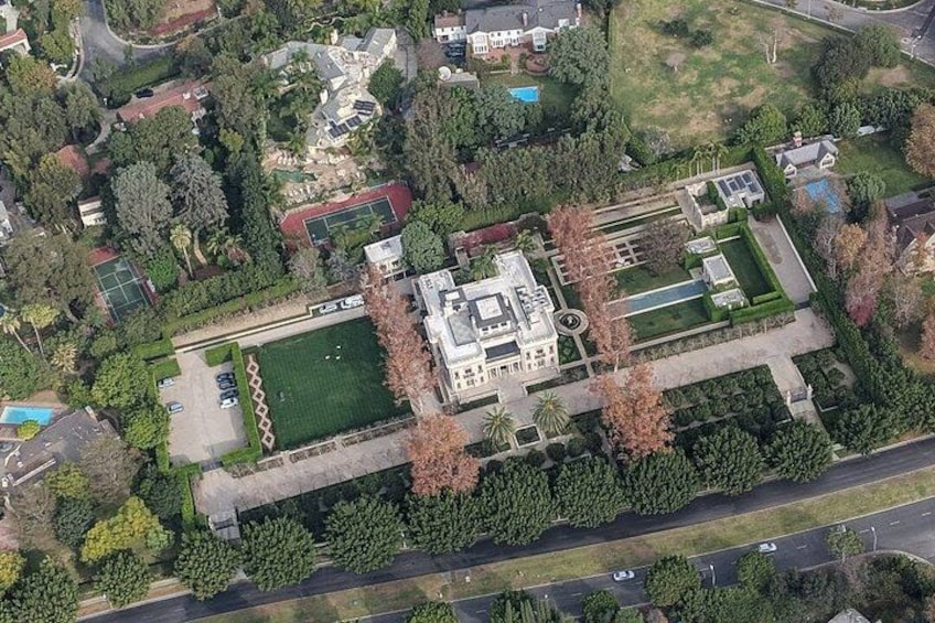 Vista aérea de una extensa propiedad con un edificio central, rodeada de jardines ajardinados, una cancha de tenis y una piscina. 4