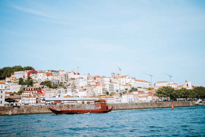 A coastal cityscape with a prominent red boat on the water, buildings with red roofs, and construction cranes in the background. 2