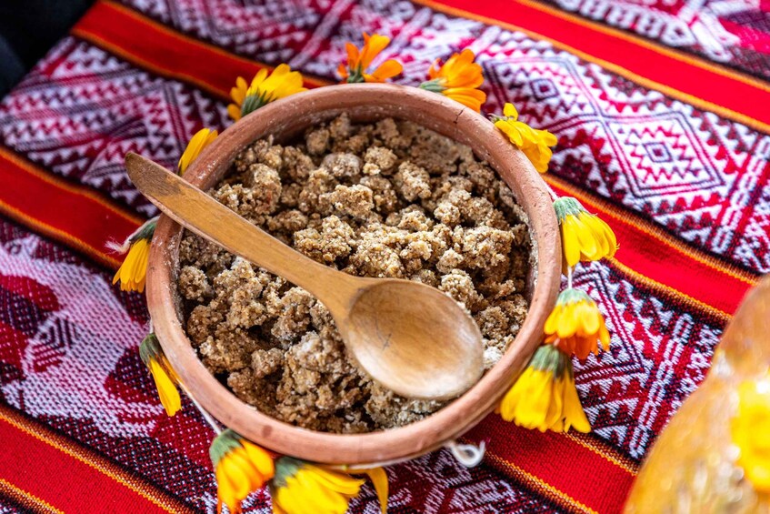 A bowl of food with a wooden spoon, surrounded by colorful flowers and a patterned fabric. 2