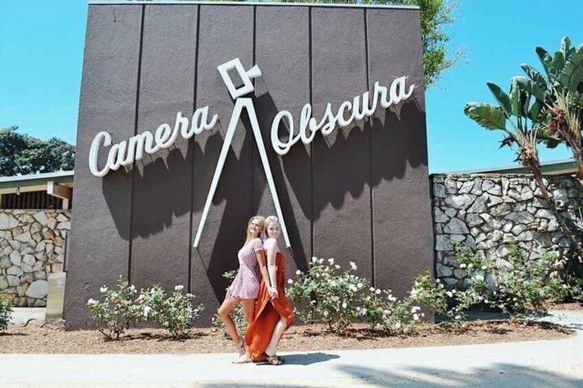A woman in a pink dress standing in front of a sign that reads 'Camera Obscura.' 3