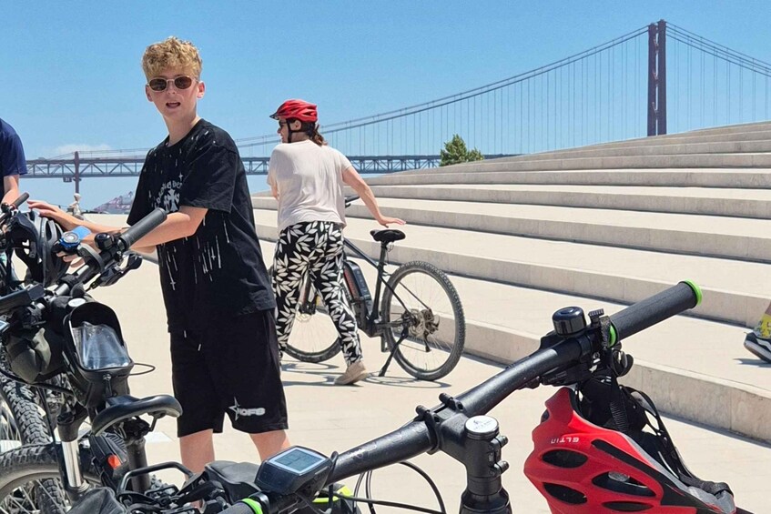 En person med en cykel og en motorcykel, en bro i baggrunden og trapper, der fører op til broen. 4