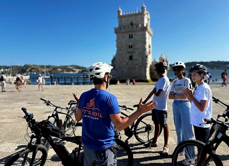 En gruppe mennesker med cykler ved en historisk tårn nær havet. 1